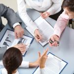 employees gathered around a table talking and pointing at reports