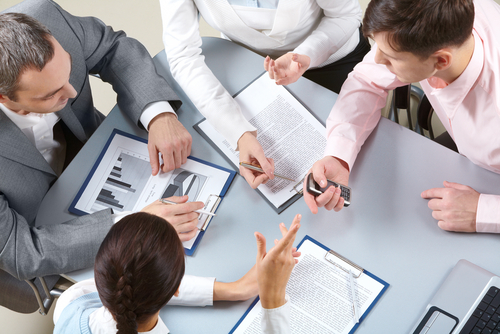 employees gathered around a table talking and pointing at reports