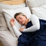 a woman sleeping on a mattress with a blue blanket