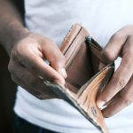 person holding brown leather bifold wallet after overspending.