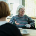 a woman sitting at a table talking with her senior mom across the table; loved ones changing needs