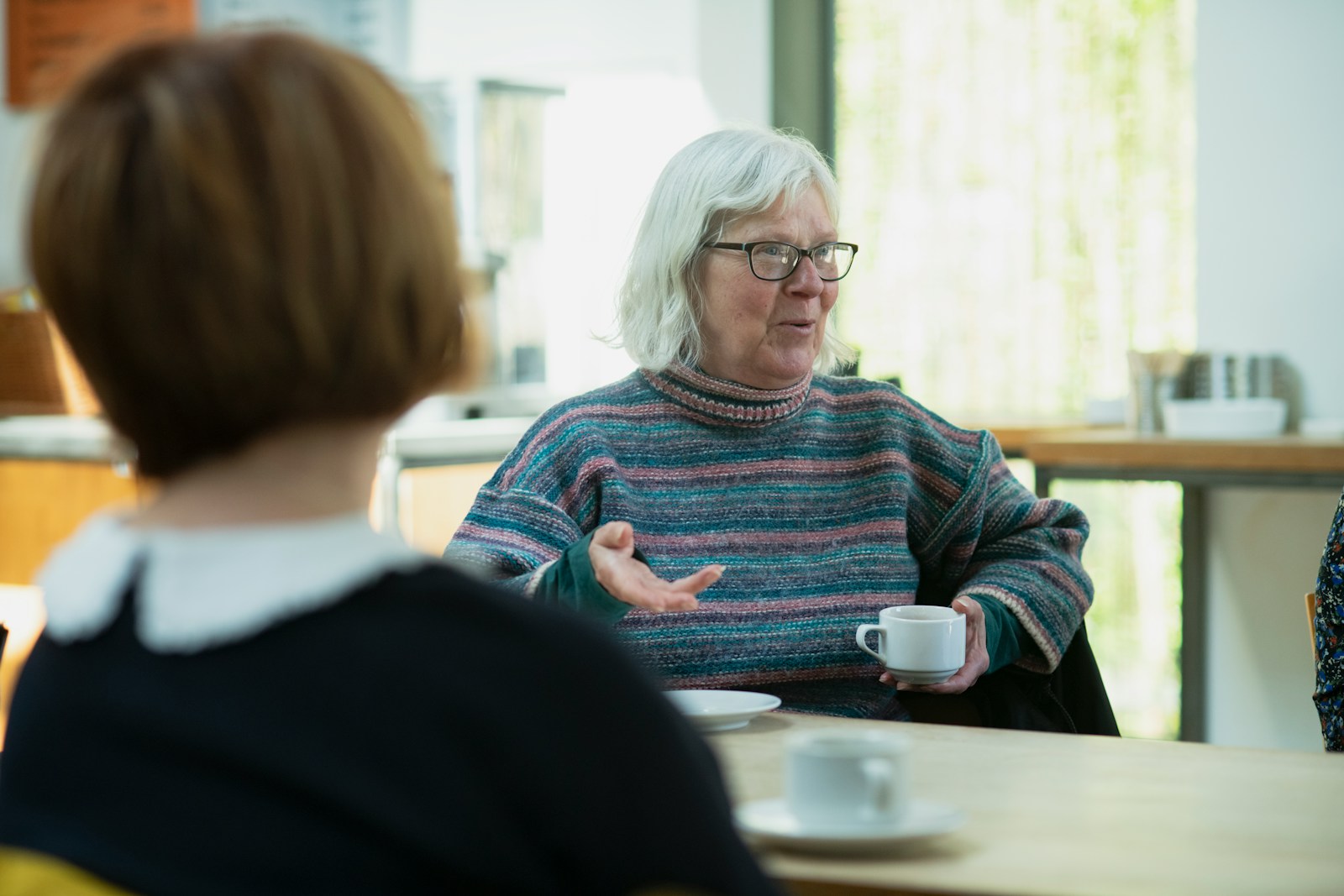 a woman sitting at a table talking with her senior mom across the table; loved ones changing needs