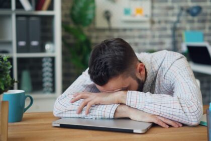 a man sitting at a desk with his head in his hands; ambition turns against you