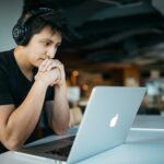 Entrepreneur wearing headphones while sitting at desk watching a training video on MacBook; transferable skills entrepreneurship