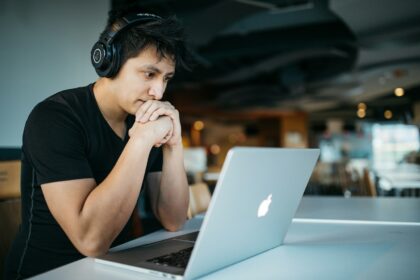 Entrepreneur wearing headphones while sitting at desk watching a training video on MacBook; transferable skills entrepreneurship