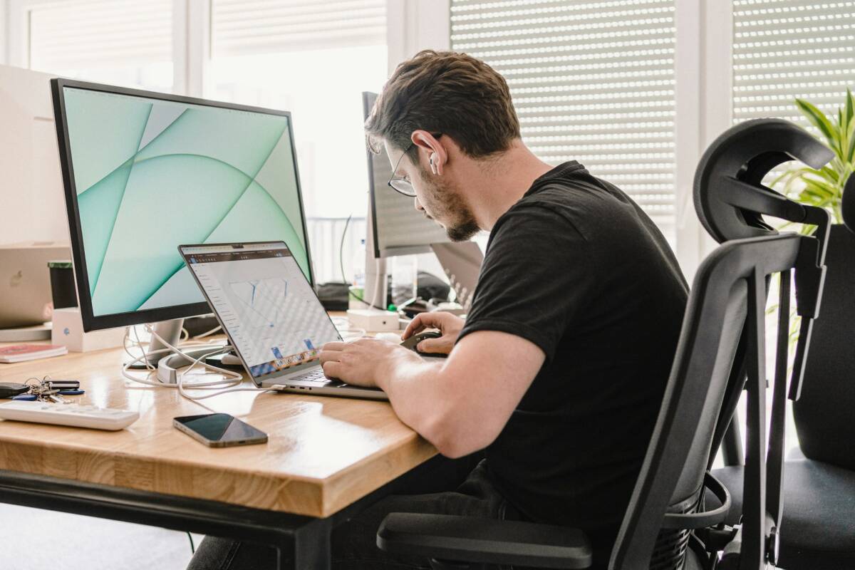 Entrepreneur sitting at work desk using a laptop and a monitor; entrepreneurs long desk hours