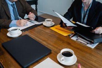 Close-up image of coworkers in formal clothes sitting at table with documents and cups of coffee while working together; paramount warner bros merger