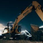 A powerful excavator at a construction site under the night sky, with workers around; construction robots