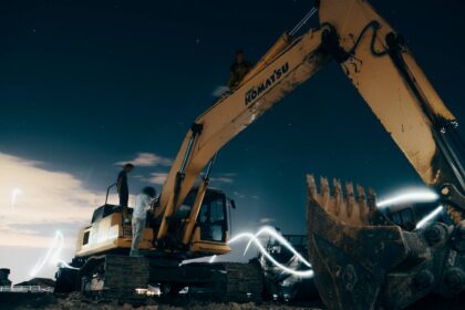 A powerful excavator at a construction site under the night sky, with workers around; construction robots