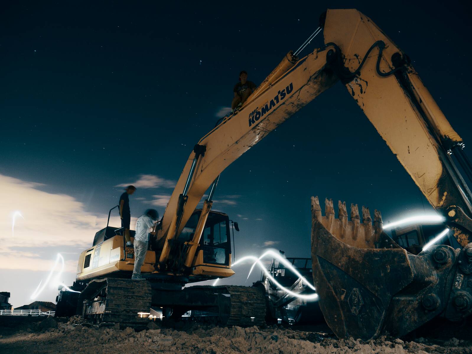 A powerful excavator at a construction site under the night sky, with workers around; construction robots