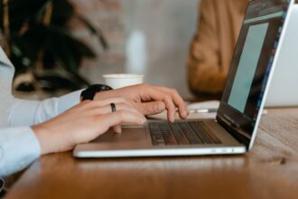 A person typing on a laptop at a wooden table in a modern office setting; ai side hustles