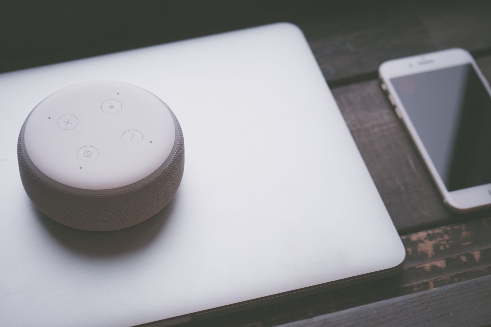 A smart speaker, laptop, and smartphone array representing modern technology lifestyle on a wooden surface; ai voice models